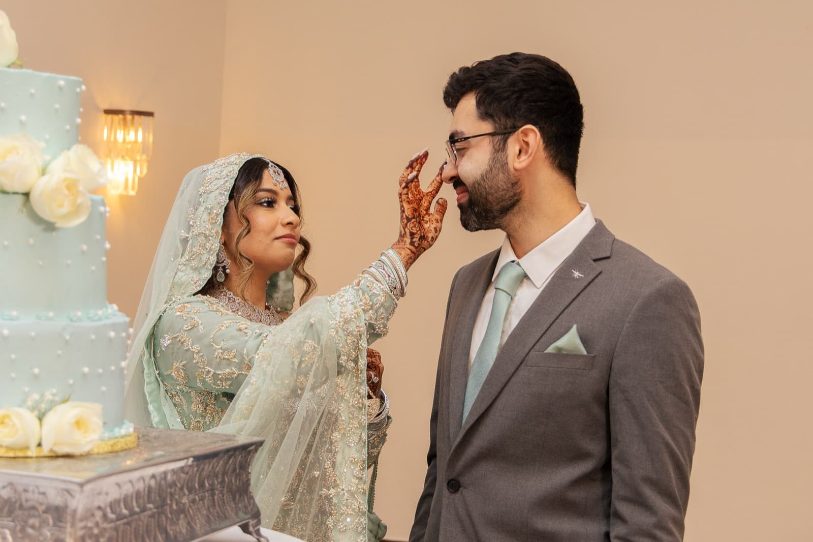 Bride booping frosting onto her groom's nose at the cake table, henna hands mid-mischief