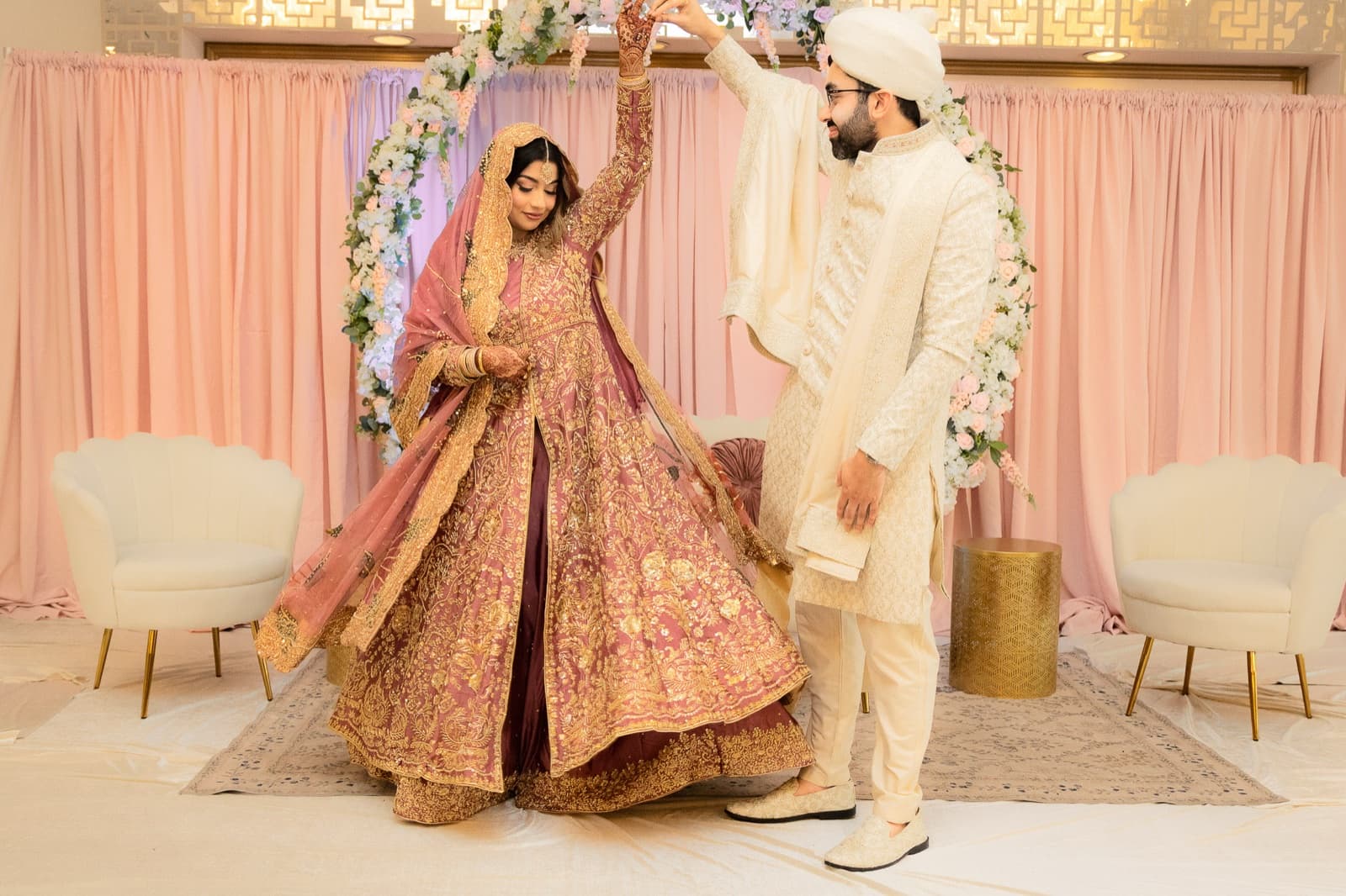 Bride and groom in a close embrace against the blush backdrop, mid-laugh