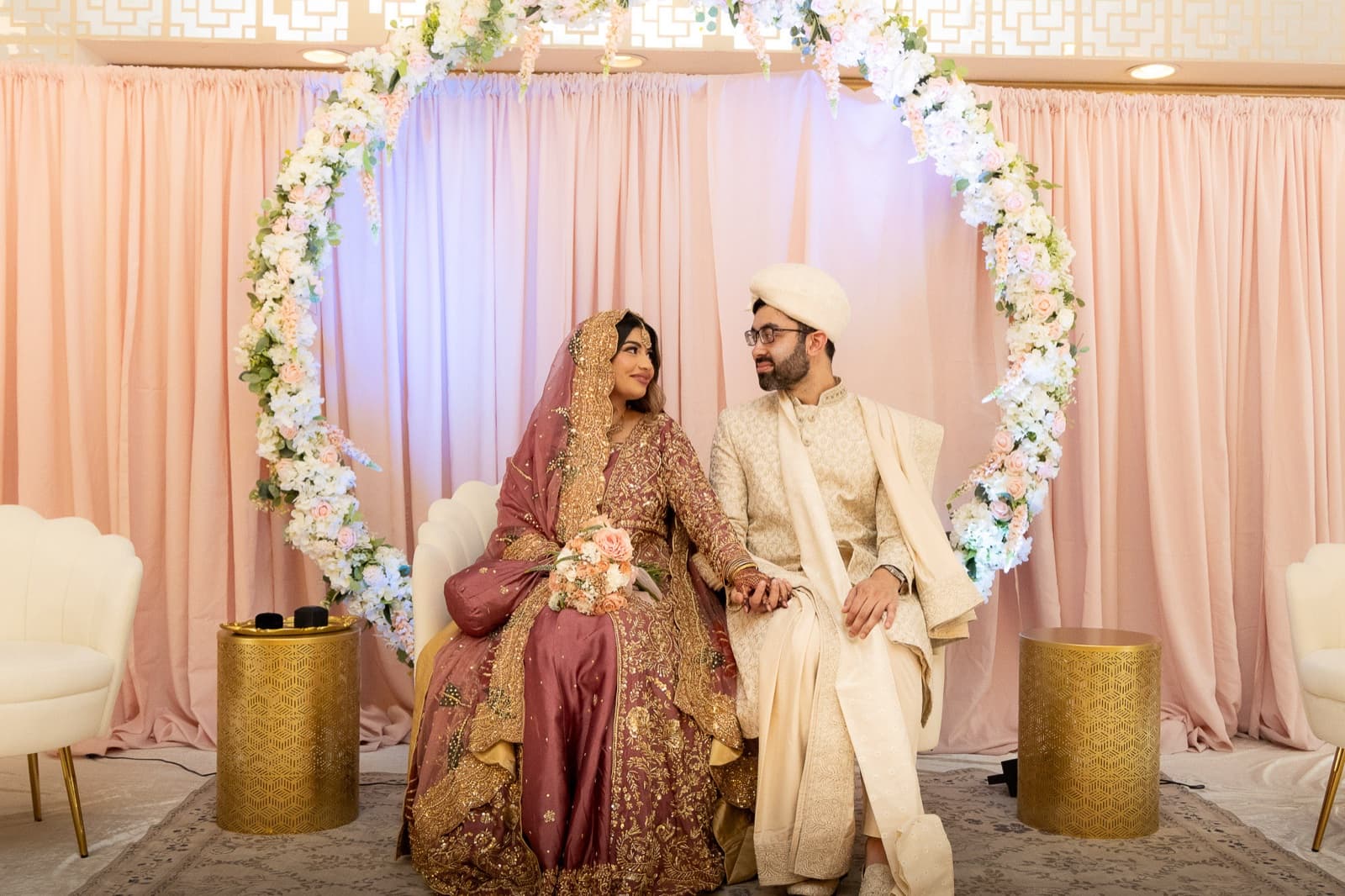 Seated together inside a circular floral arch against the blush pink backdrop