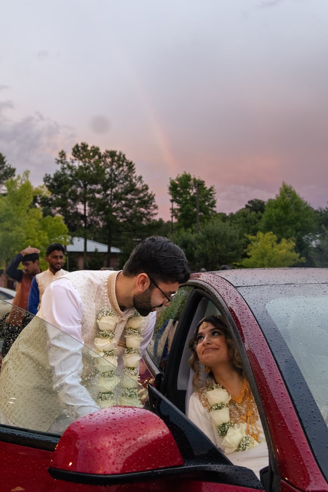 Groom leaning into the send-off car for one more look at his bride, a rainbow breaking in the sky behind