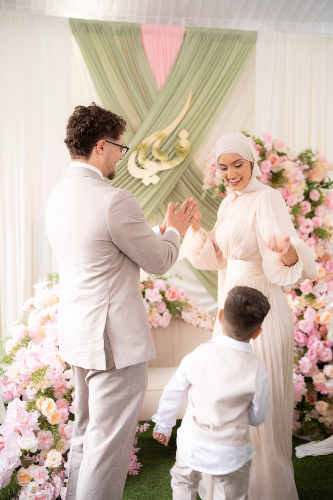 Couple celebrating on the flower-lined stage, a little boy in white looking up at them