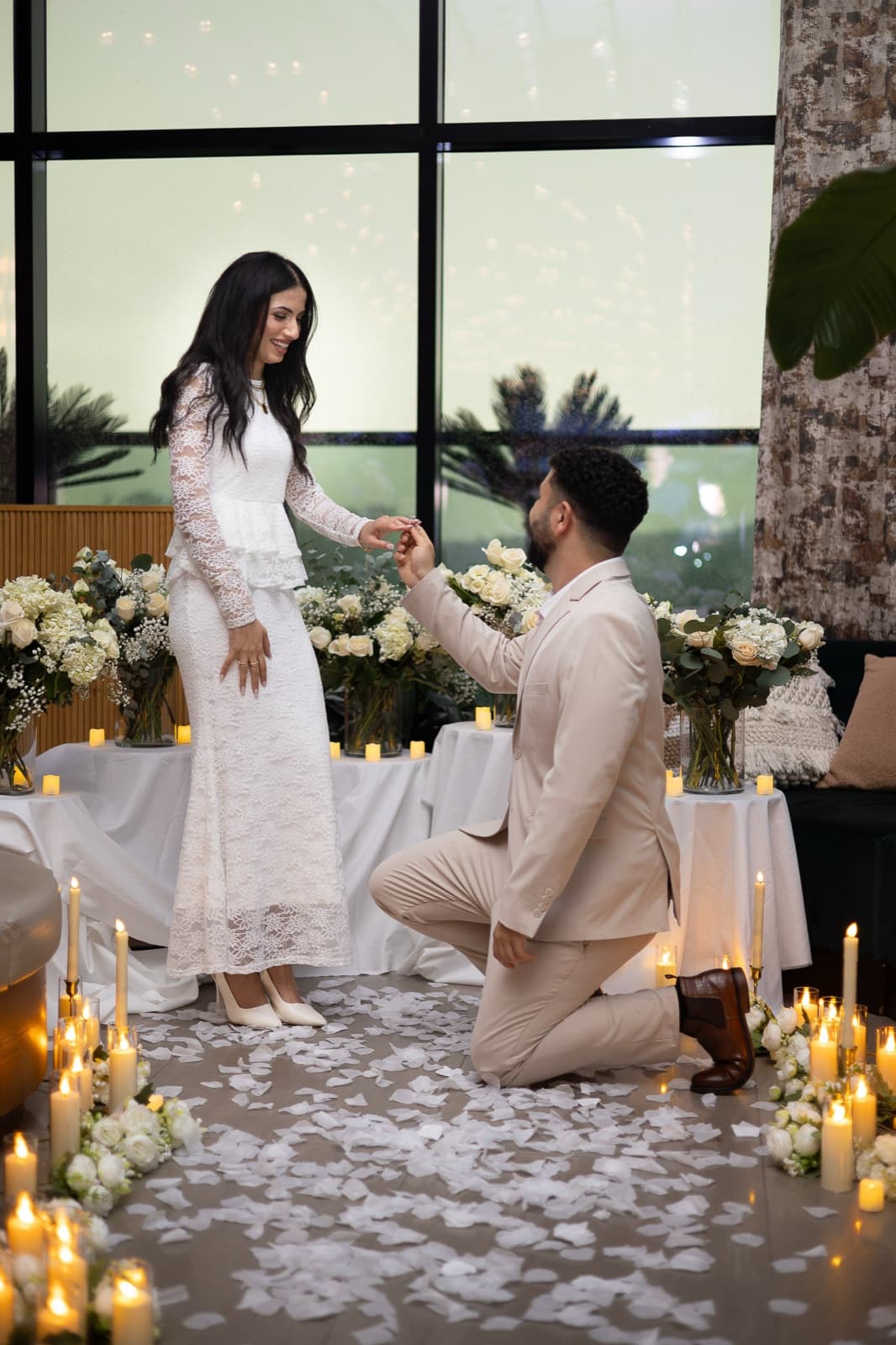 The proposal: down on one knee among candles and white rose petals, her hand over her mouth