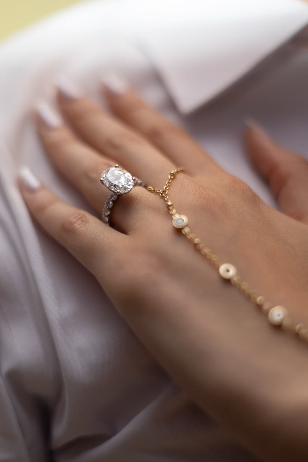 Close-up of the engagement ring and gold hand chain against the groom's white shirt