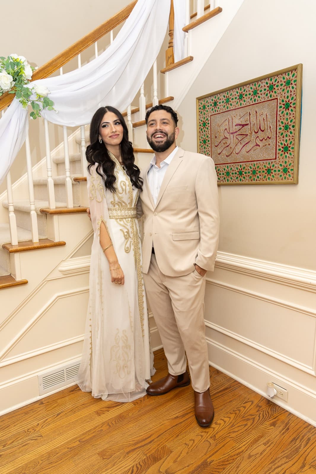 Engagement portrait at the base of the staircase, white drapery and Arabic calligraphy behind them