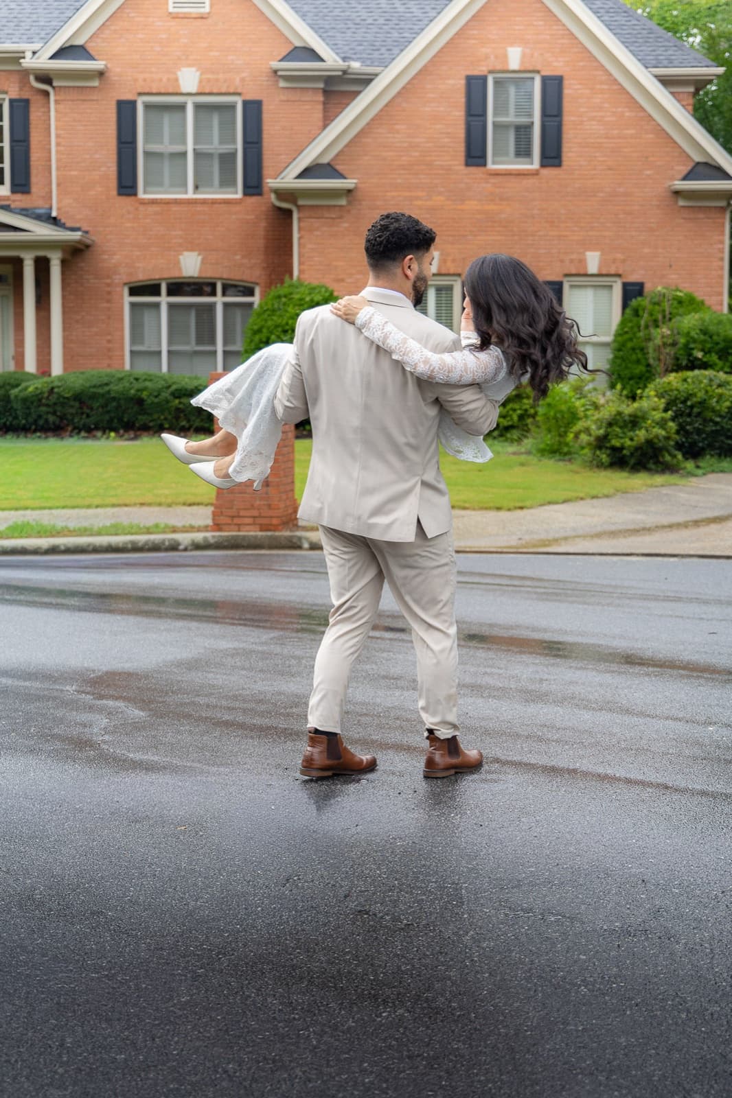 Groom carrying his bride across a rain-slicked street, her heels off the ground