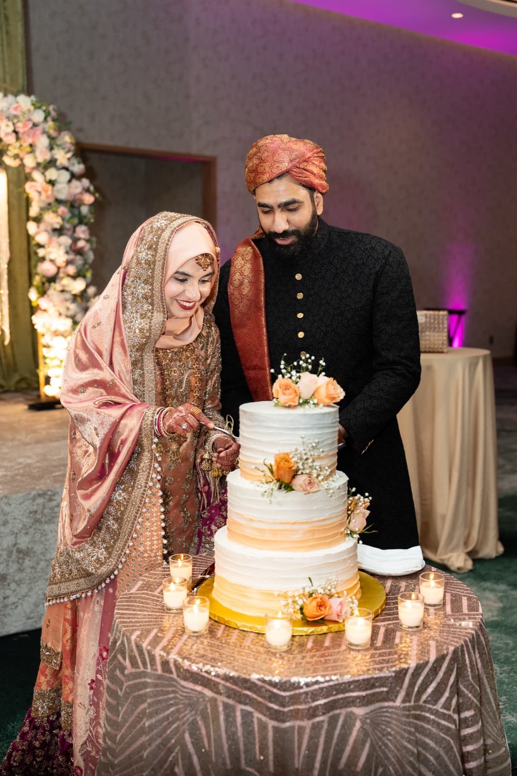Cutting the cake together by candlelight, her rose-gold shawl glowing against his black sherwani