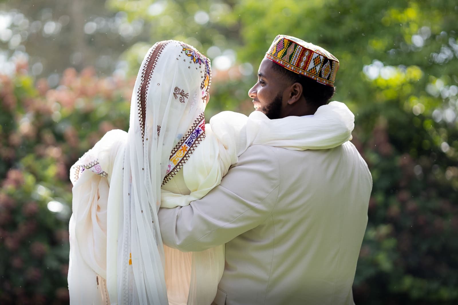 Over the bride's shoulder: the groom's embroidered kufi and a quiet embrace in the garden