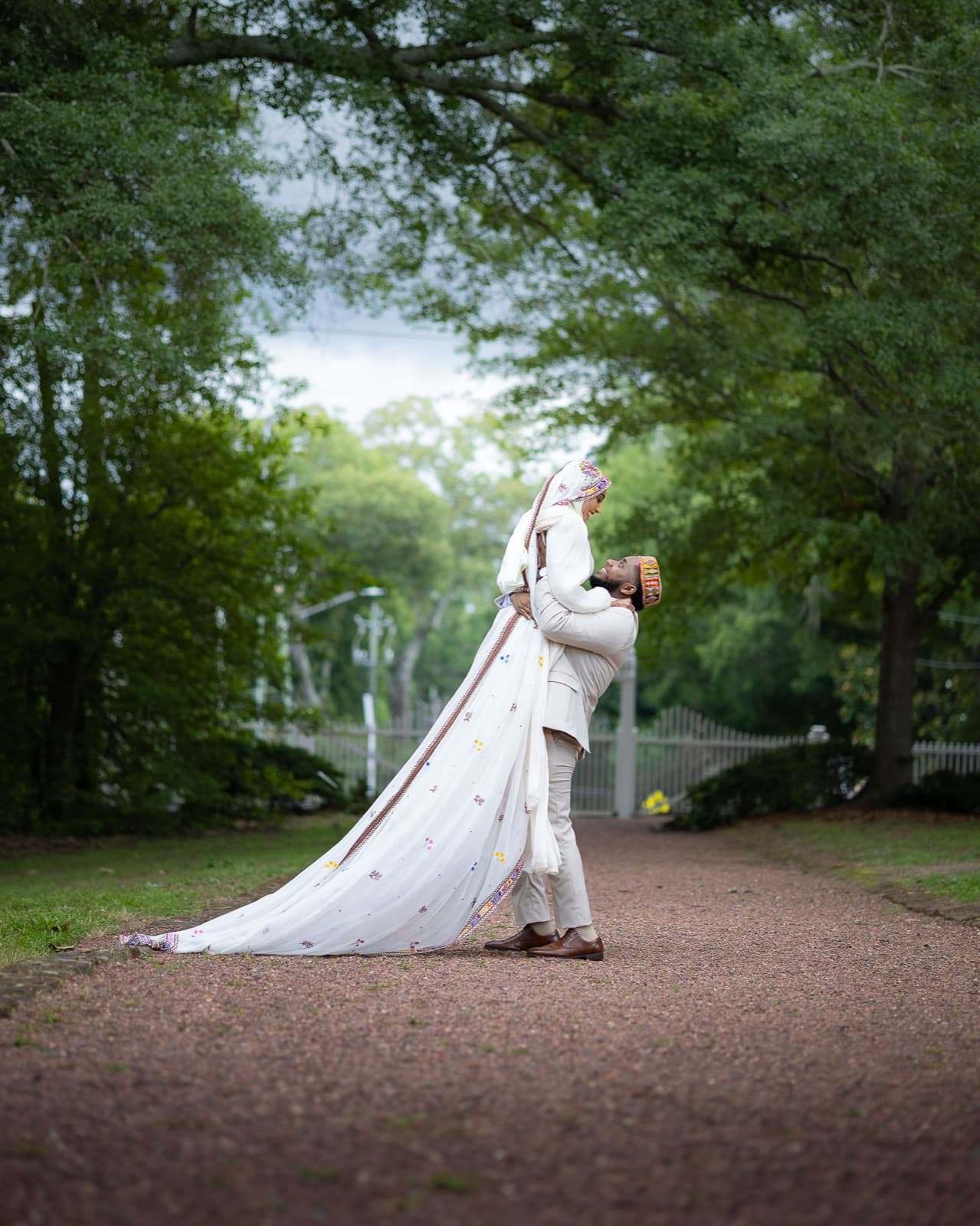 Closing image: groom lifting his bride on a tree-lined path, her embroidered veil trailing to the ground