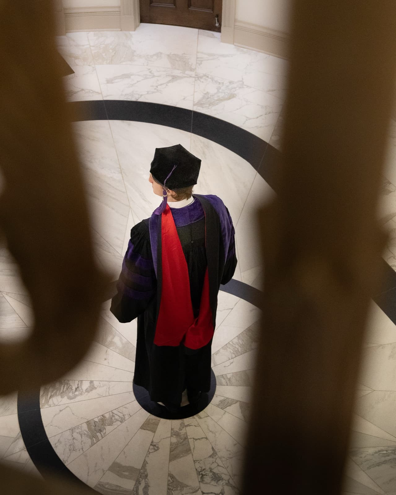 Overhead frame: law graduate standing on the marble rotunda floor in JD regalia