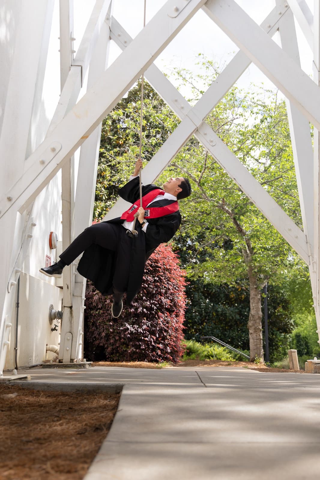 Graduate swinging off the ground on the UGA Chapel Bell rope, gown flying