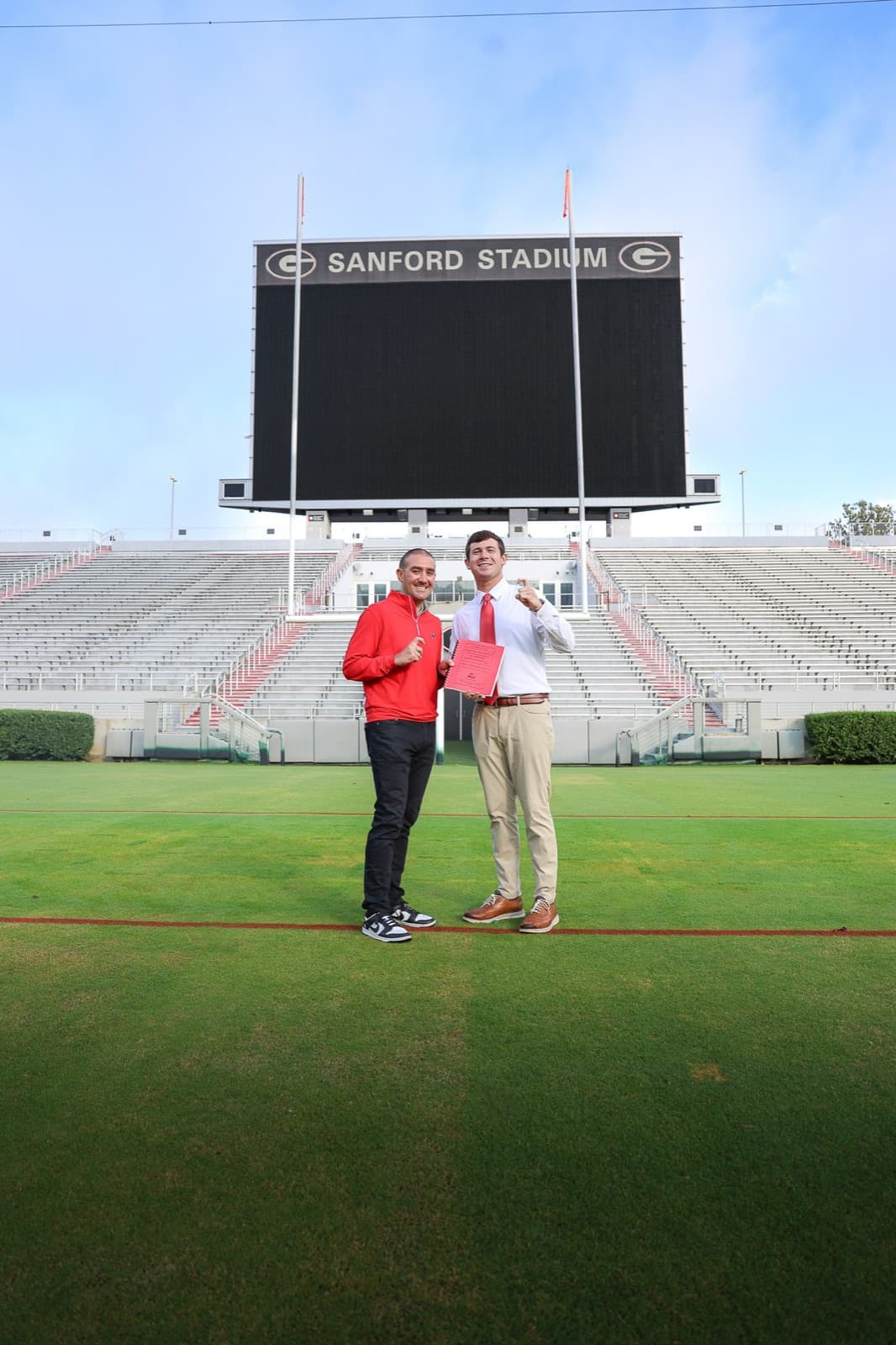 Graduate and his dad side by side on the field under the Sanford Stadium scoreboard