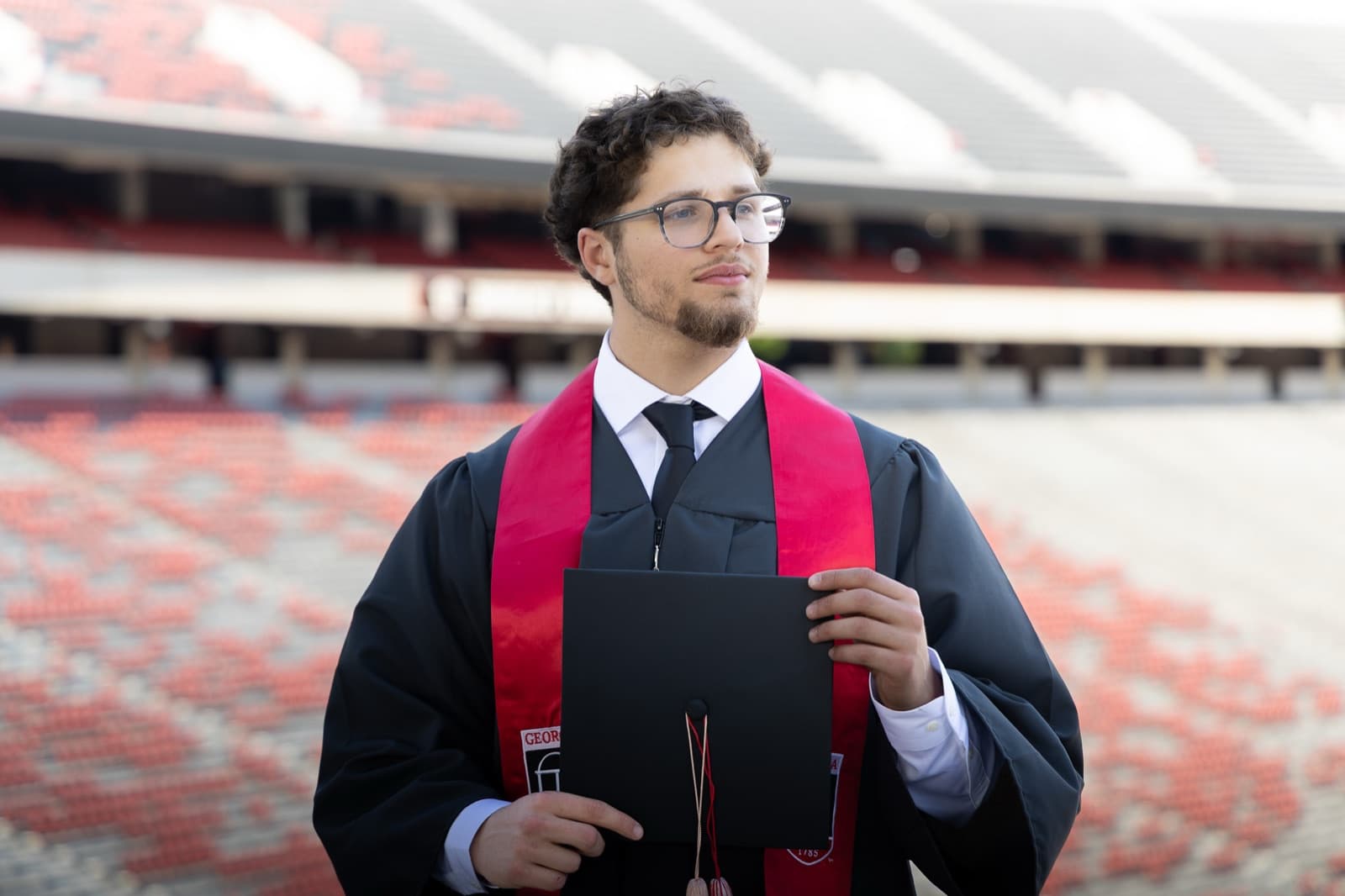 Graduate laughing with his diploma cover at Sanford Stadium, red UGA stole