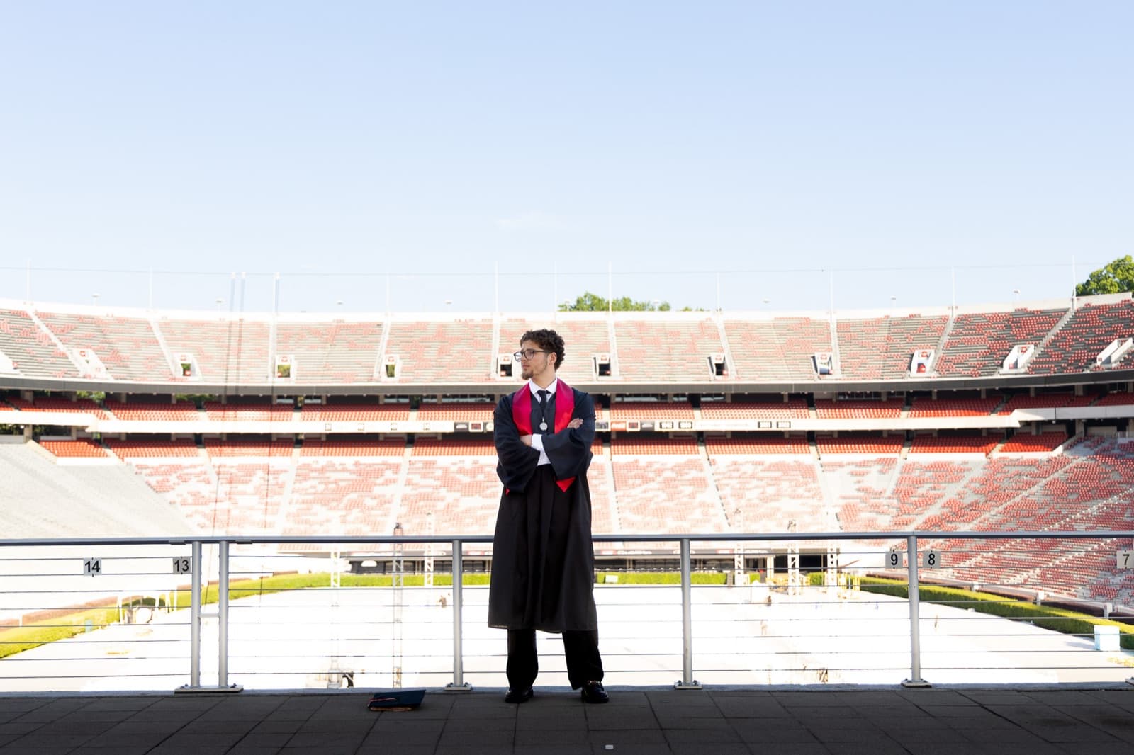 Wide shot: graduate alone at the rail of an empty Sanford Stadium