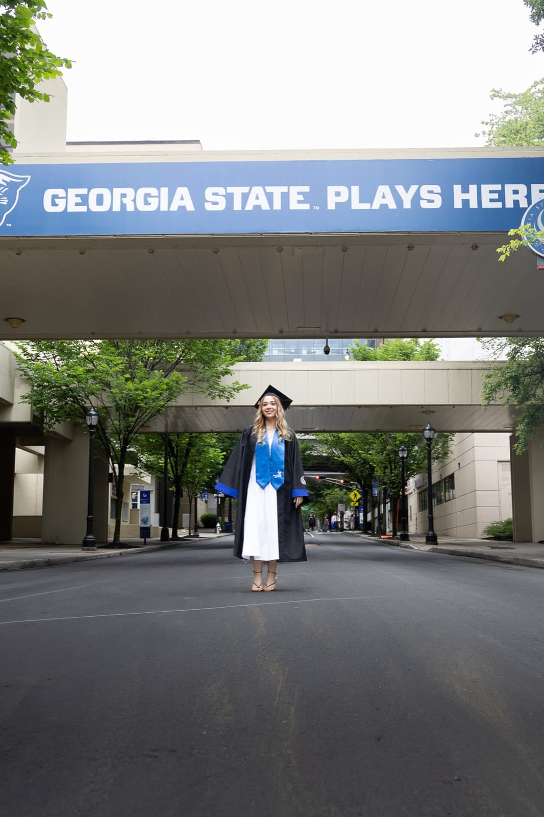Grad in cap, gown, and blue stole under the Georgia State bridge downtown
