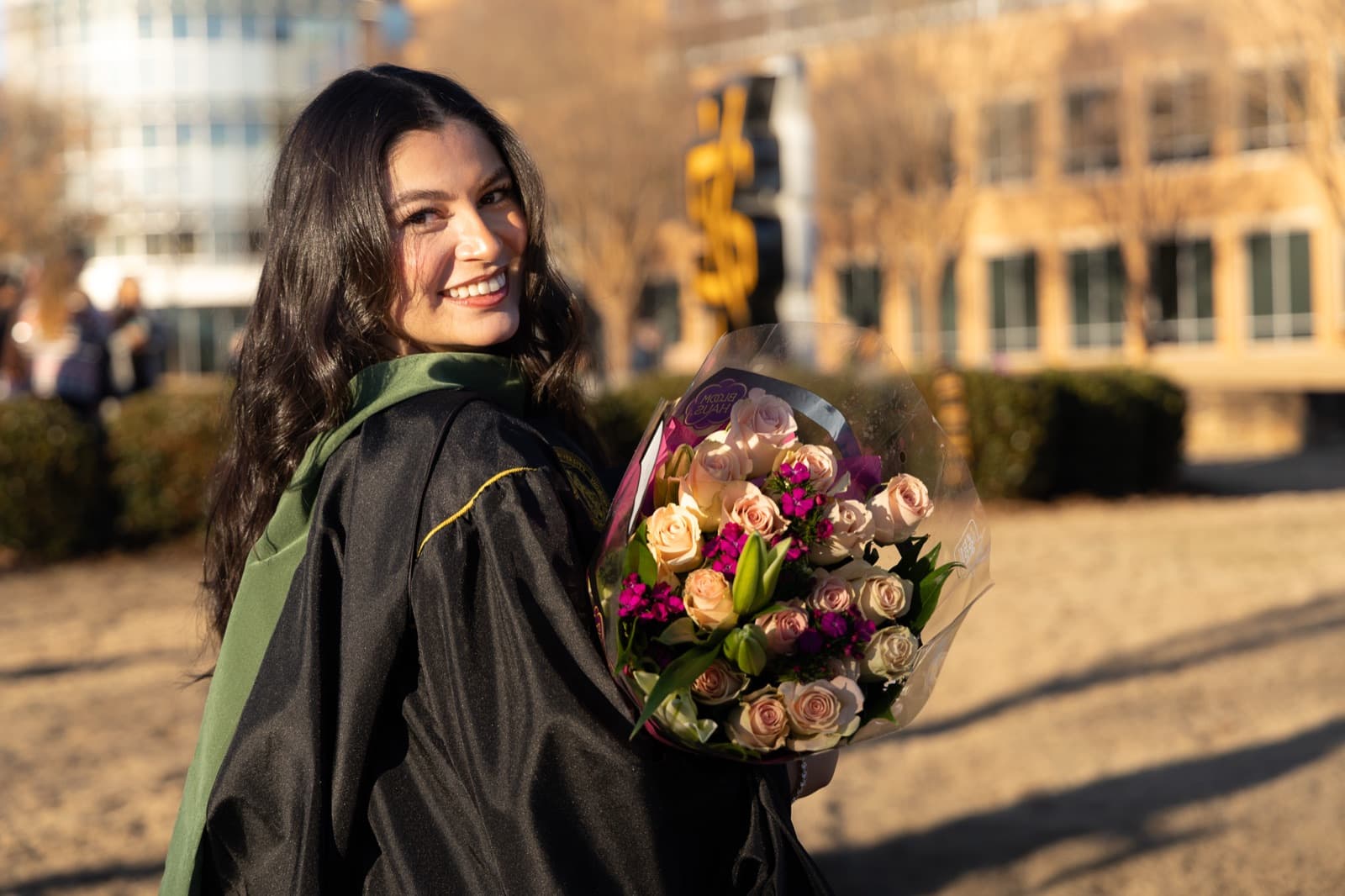 Grad glancing over her shoulder with a rose bouquet at golden hour on the Kennesaw State green