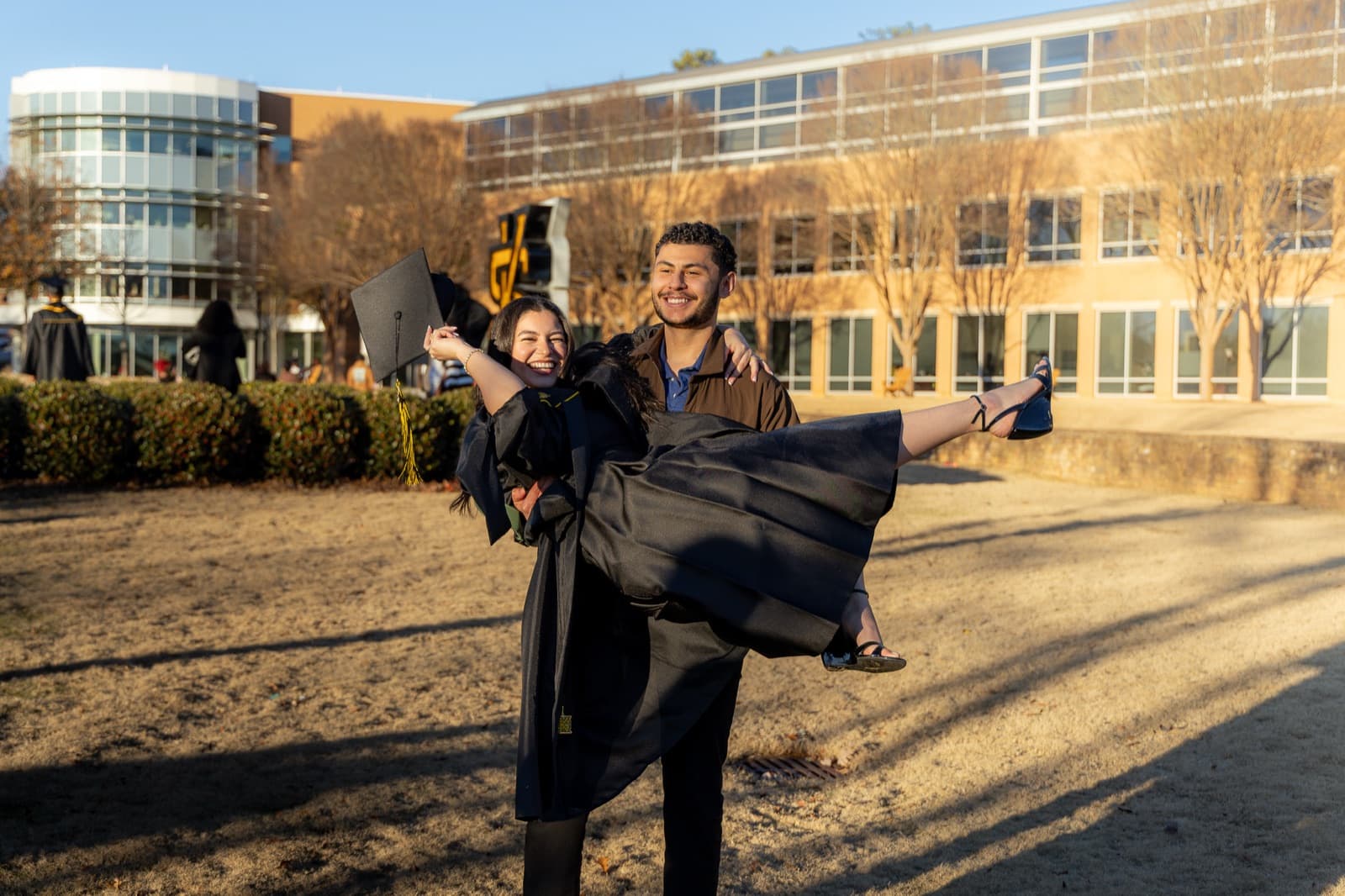 Grad swept off her feet mid-laugh, cap in hand, on the Kennesaw State lawn