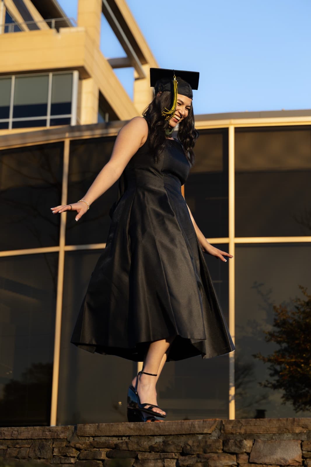 Closing image: grad twirling her dress on a stone wall at sunset, Kennesaw Hall behind