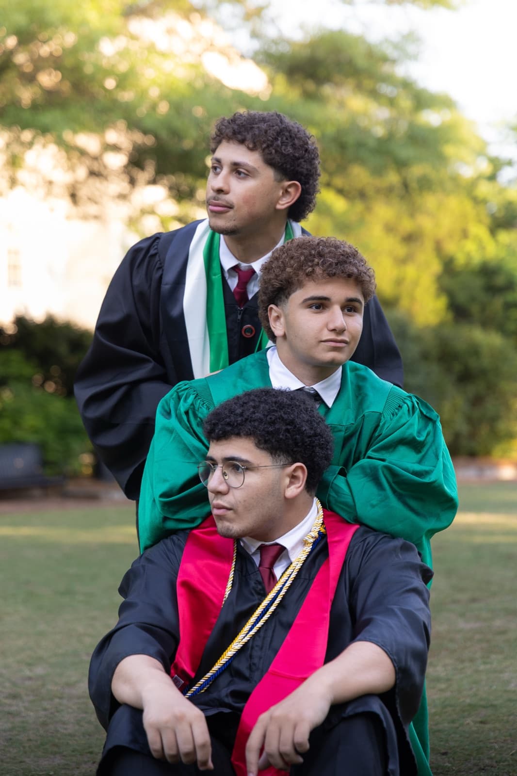 Three grads stacked in a laughing pile on the lawn, green and black gowns