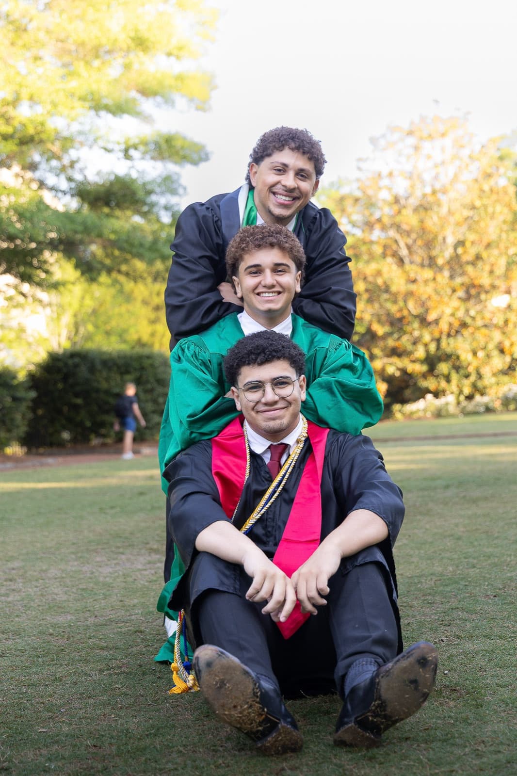 Three friends in gowns stacked up and laughing on the quad
