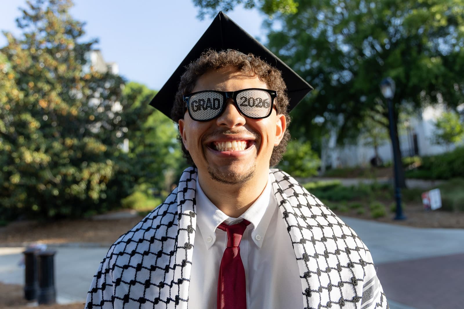 Close-up grin in novelty GRAD glasses, keffiyeh draped over the shoulders