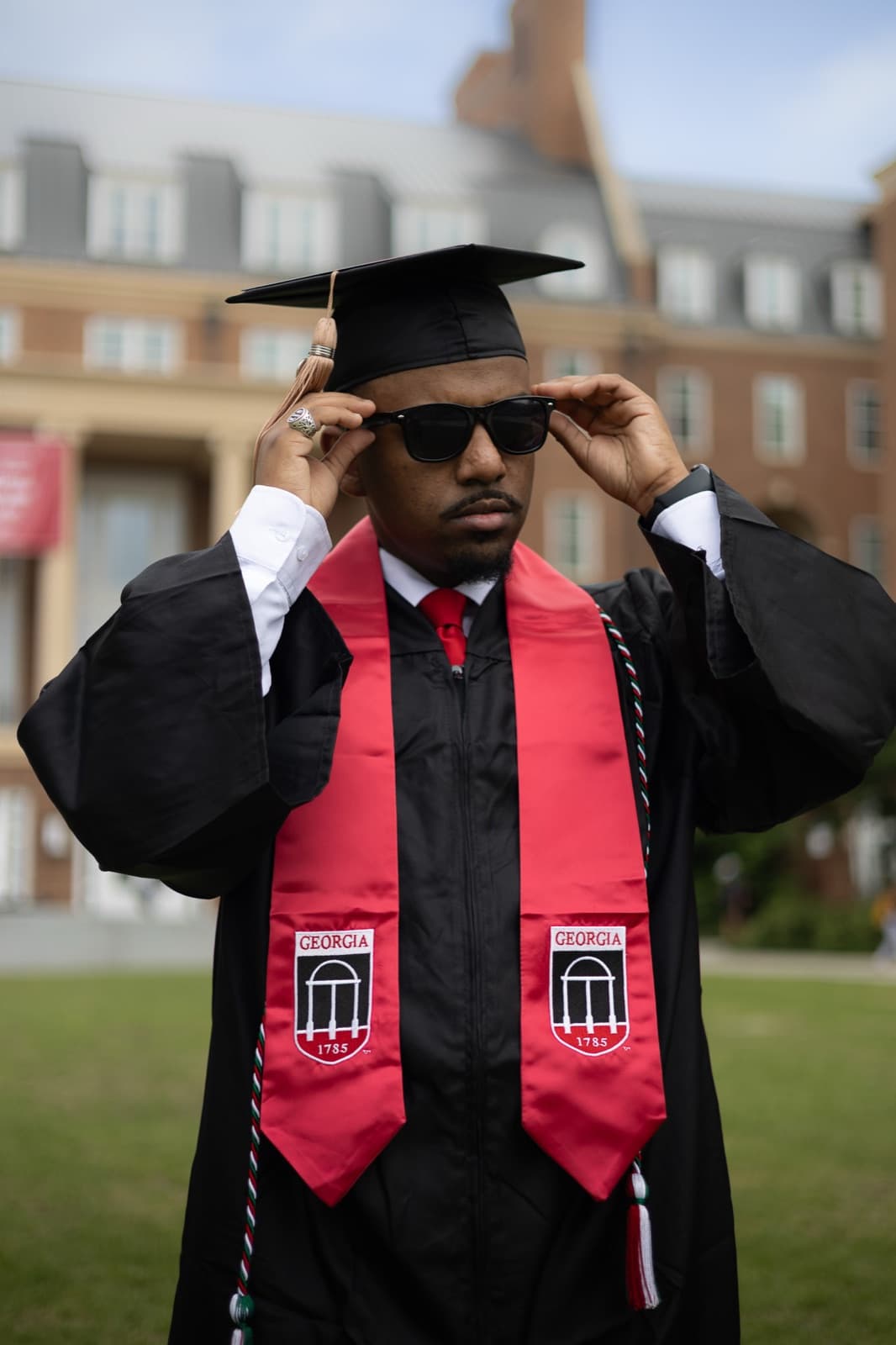 Terry College grad adjusting his sunglasses, red UGA stole over his gown