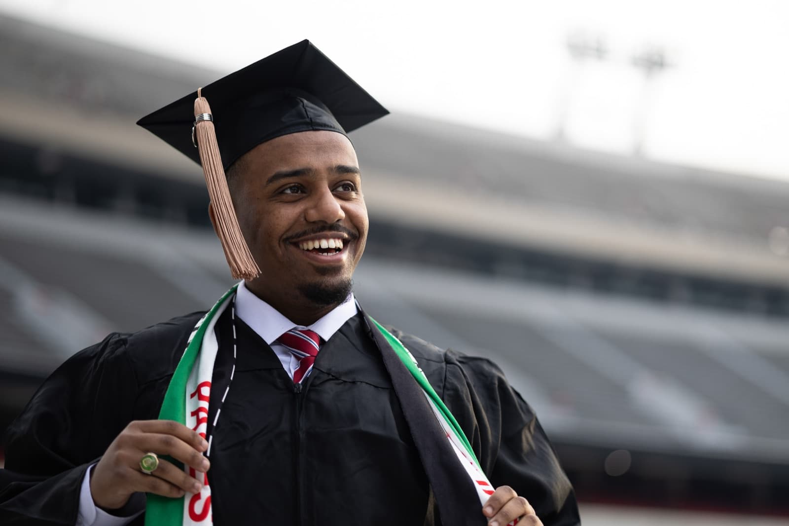 Graduate laughing over his shoulder in the stands, green and white stole