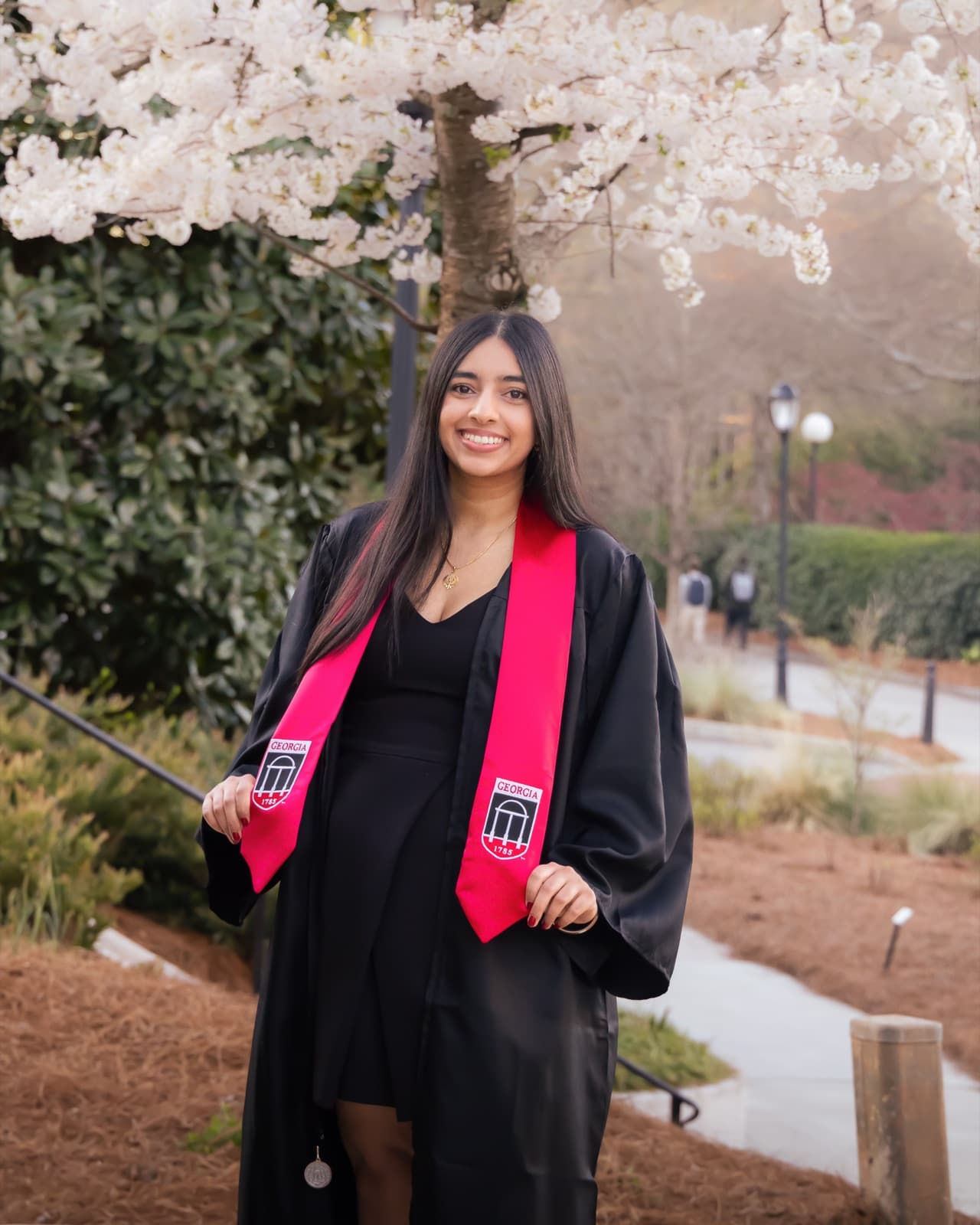 Grad in her gown under the cherry blossoms, red stole with the Arch crest